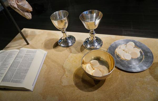 Abendmahl auf Altar. Links im Bild eine aufgeschlagene Bibel. Weiter im Bild zwei Abendmahlskelche, sowie Schalen mit Hostien.